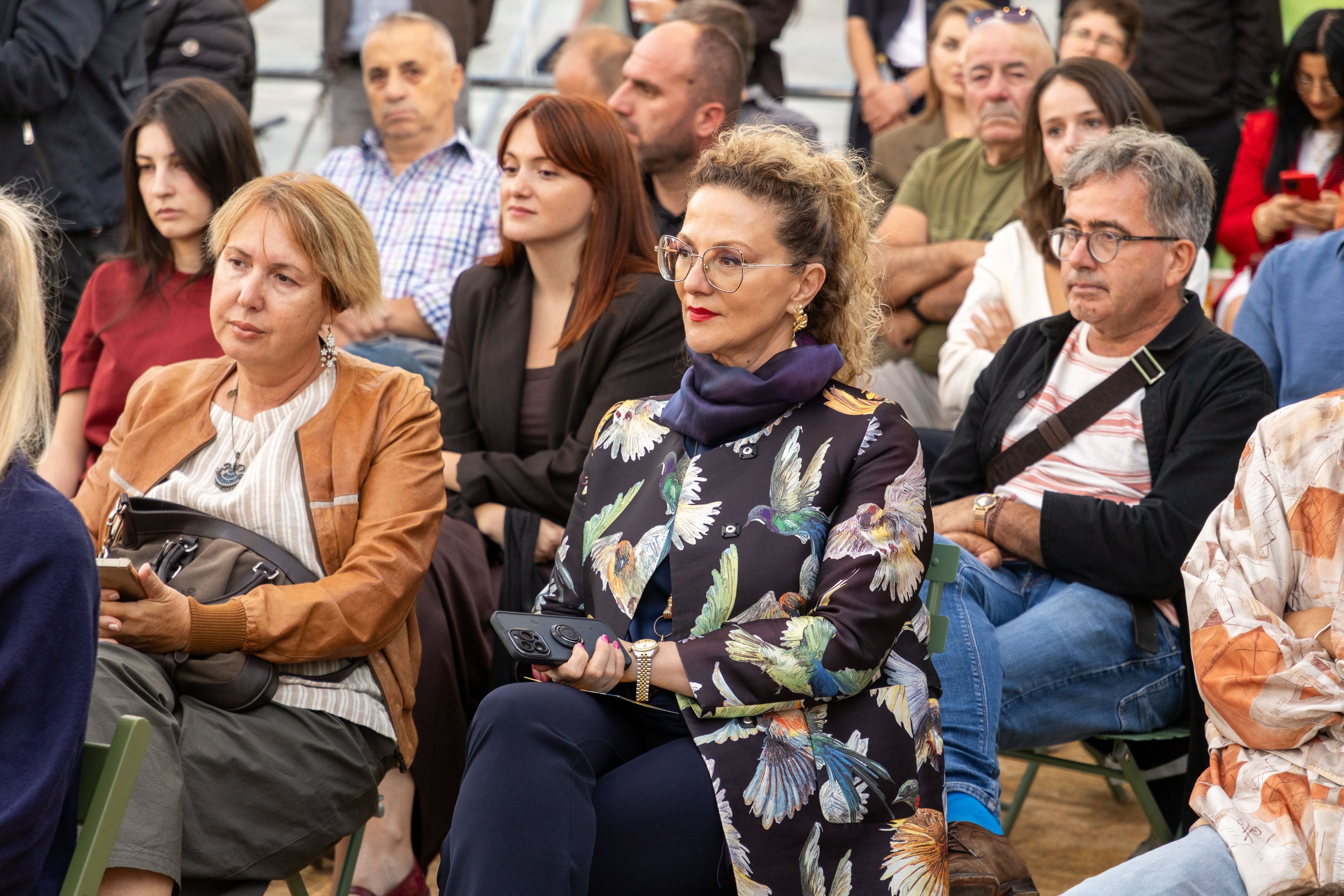 Pjesëmarrës të ulur në publik duke ndjekur ceremoninë.